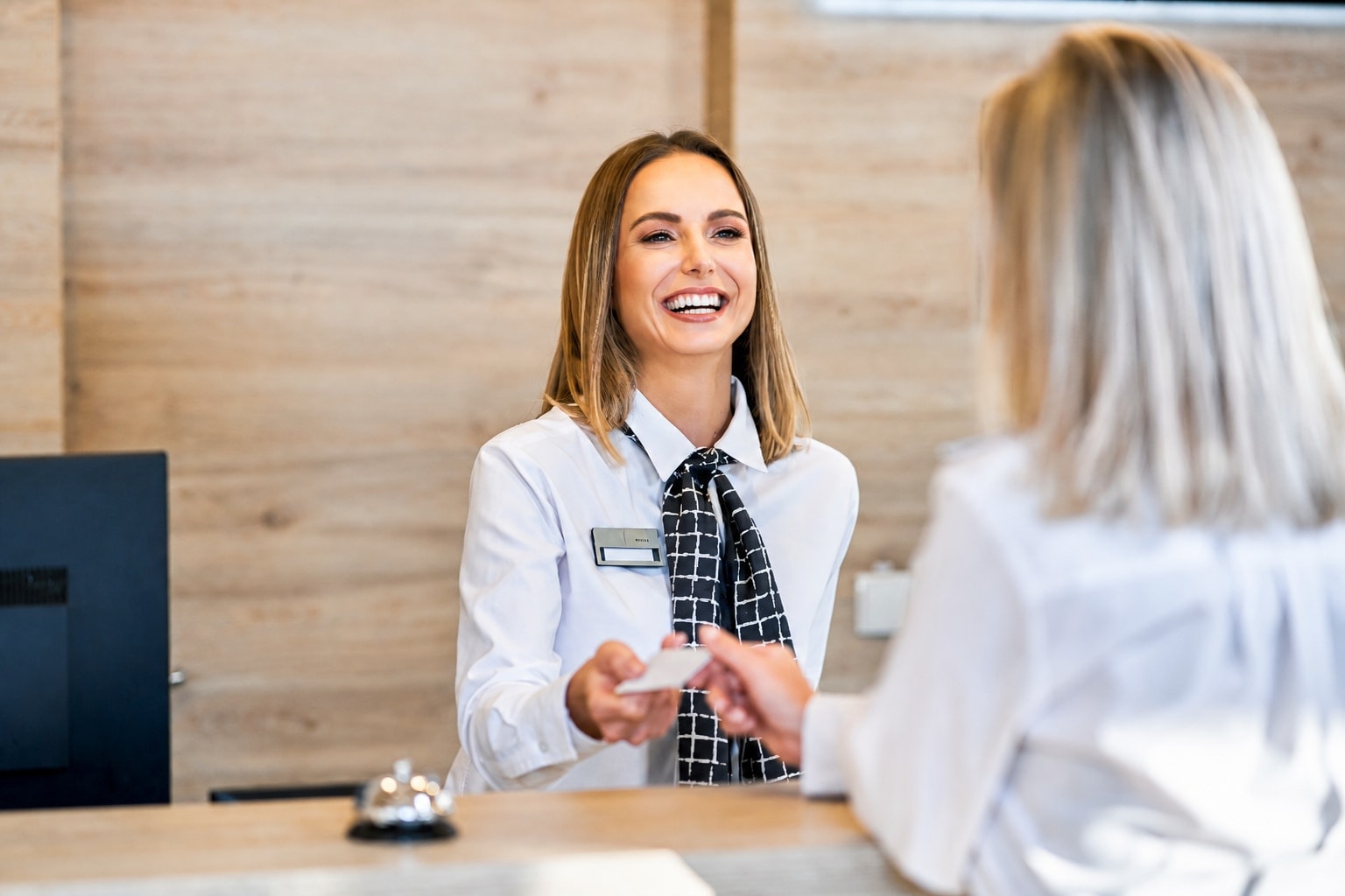 A friendly hotel receptionist in a white uniform handing a room key card to a guest at a wooden check-in desk.